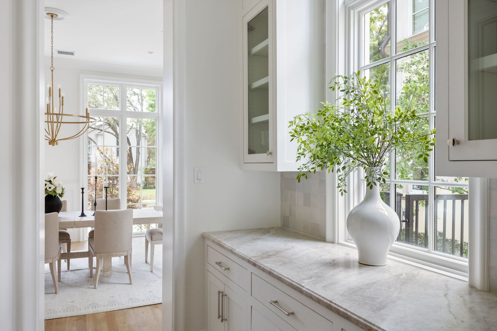 A white vase is sitting on a counter next to a window in a kitchen.