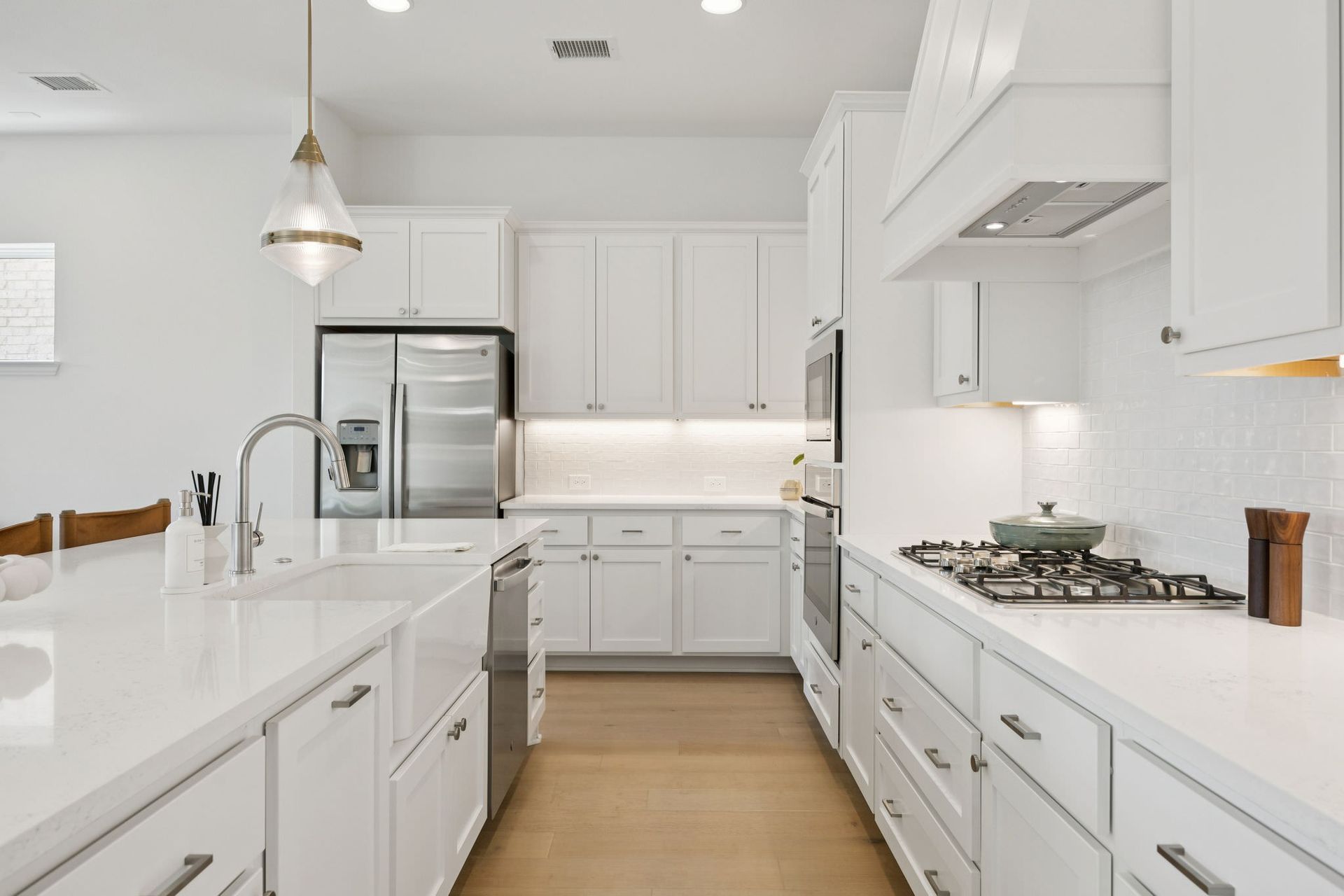 White kitchen with island, cabinets, stainless steel appliances, and wooden floor.