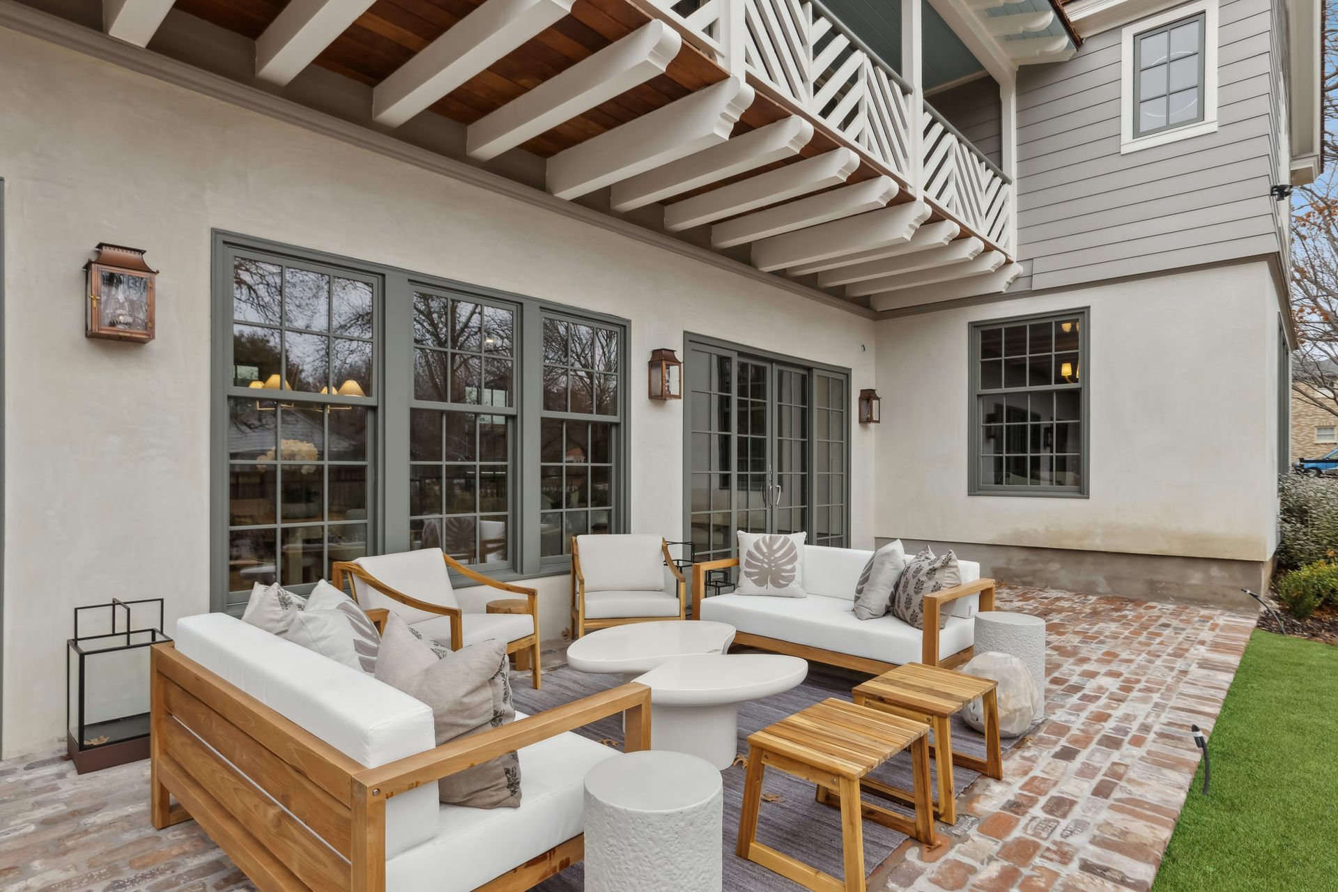 Outdoor patio with white furniture on a brick surface beneath a covered porch.