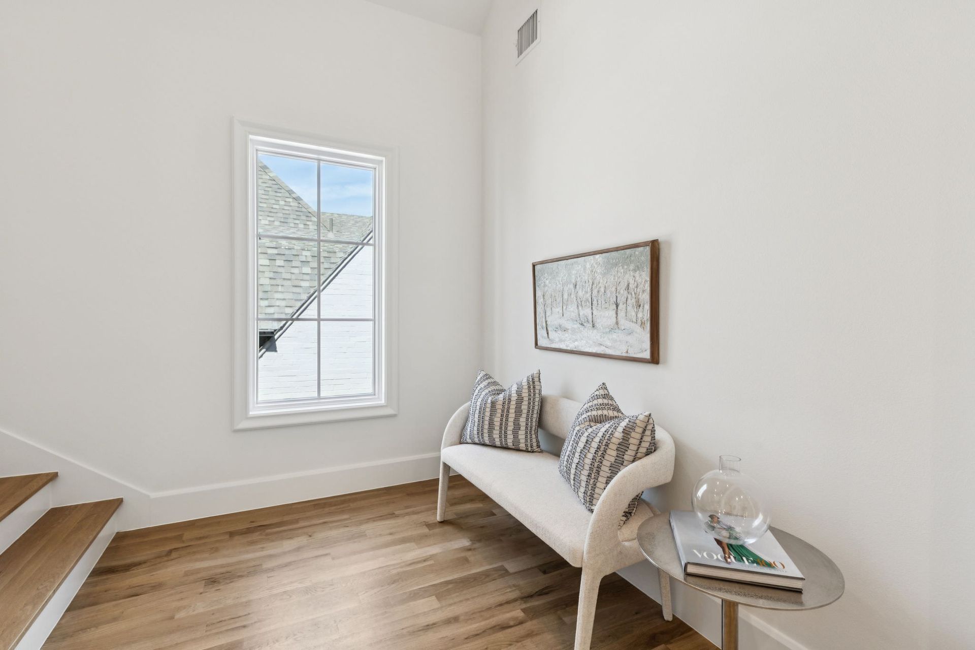 Hallway with bench, pillows, artwork, small table with books. Window with roof view.