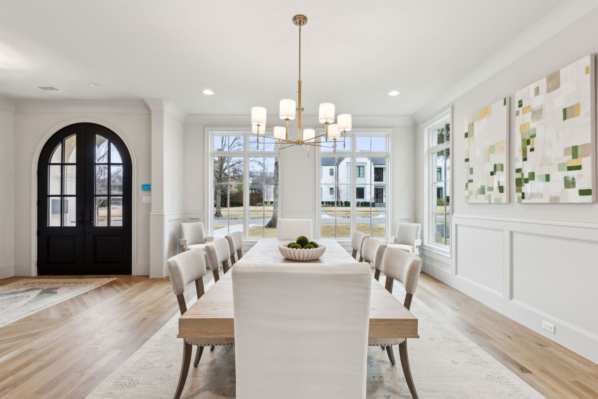 Elegant dining room with large windows, long table, white chairs, and chandelier.