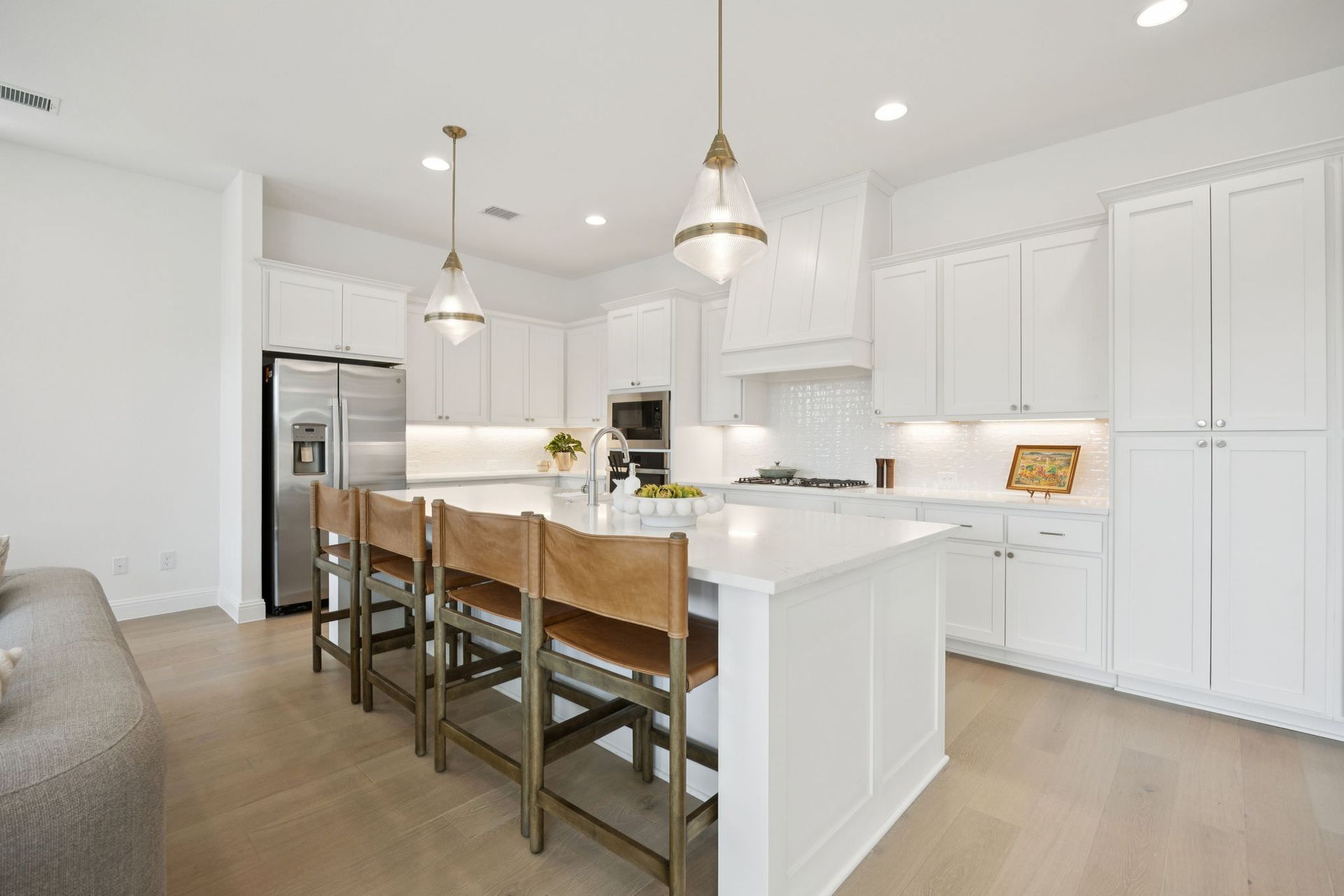 Modern white kitchen with island, stainless steel appliances, and leather bar stools.