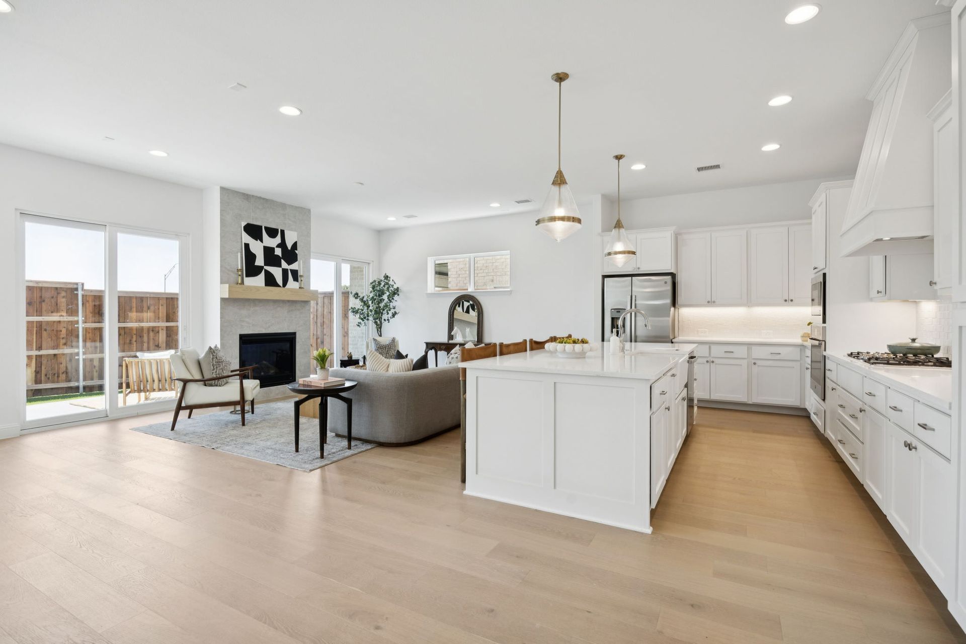 Bright, open-concept living space with kitchen island, fireplace, and light wood floors. White cabinets and walls.