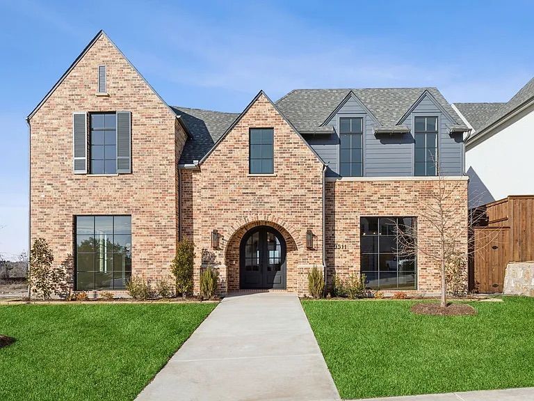 Brick house with arched doorway and grey accents, a green lawn, and a concrete walkway.