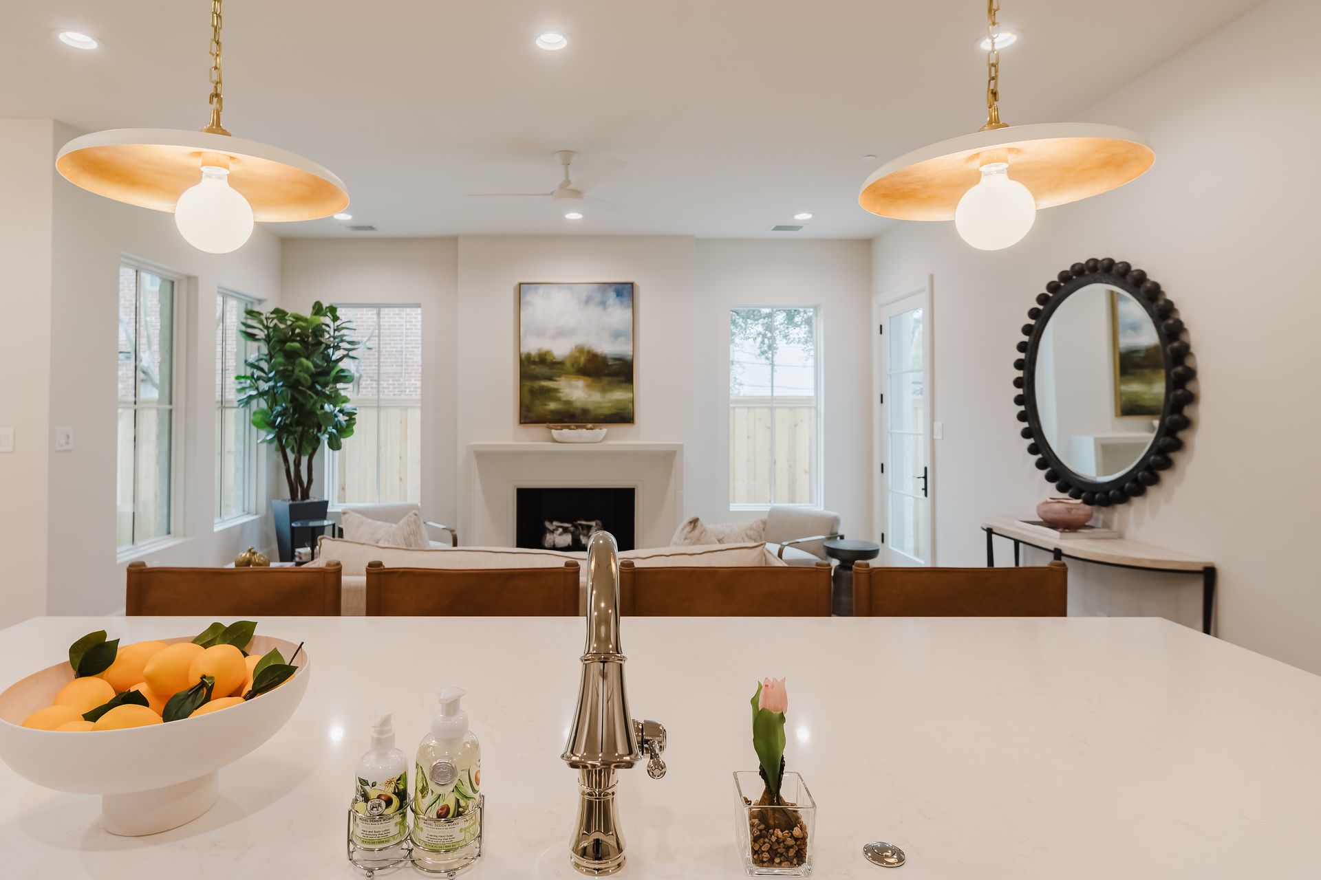 Modern kitchen with island, view into living room, neutral tones, pendant lights, and decorative bowl with citrus.