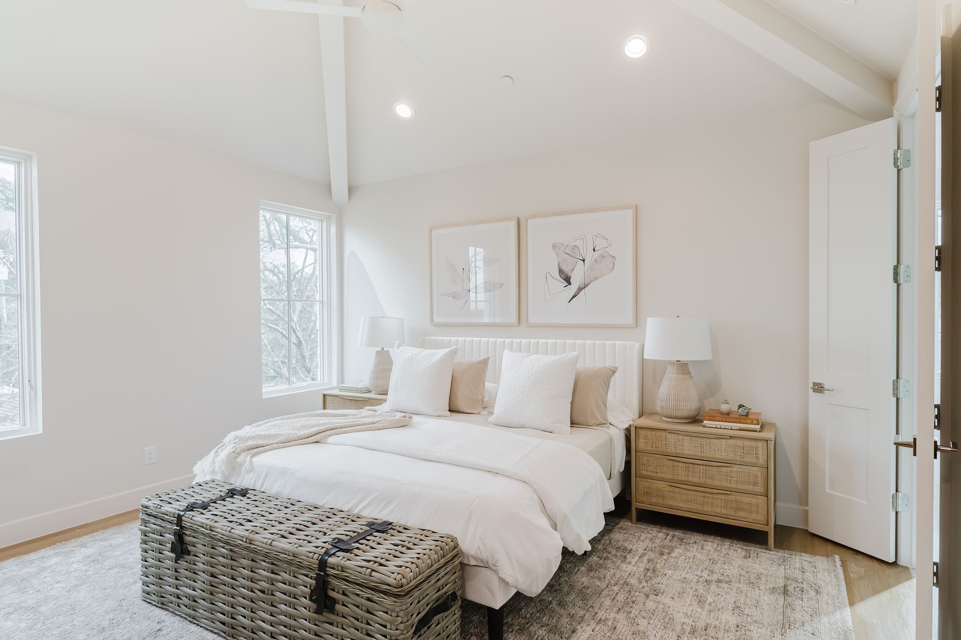 Bedroom with white walls, a bed, a trunk at the foot of the bed, and two framed prints.