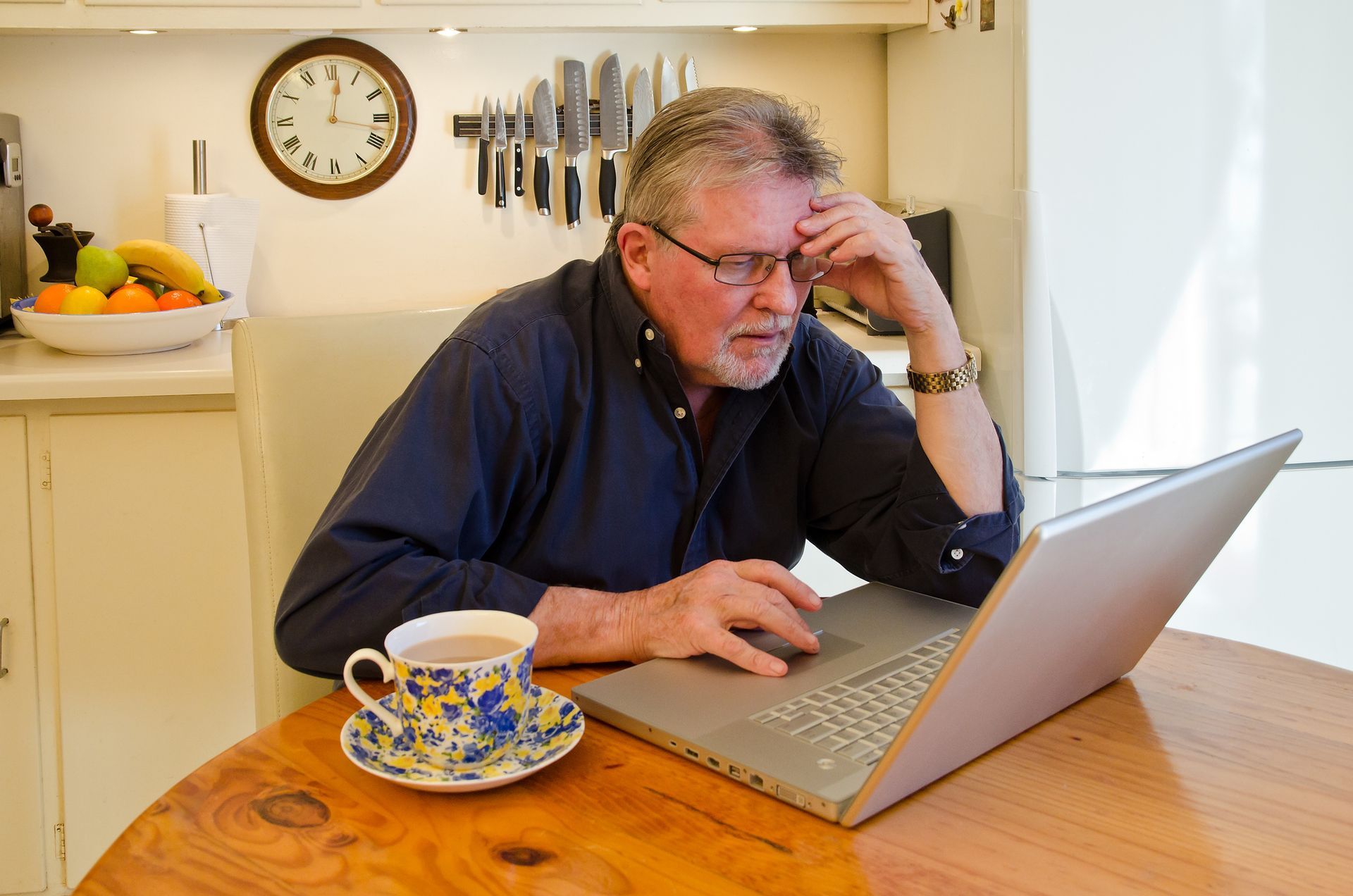 A man is sitting at a table with a laptop and a cup of coffee.