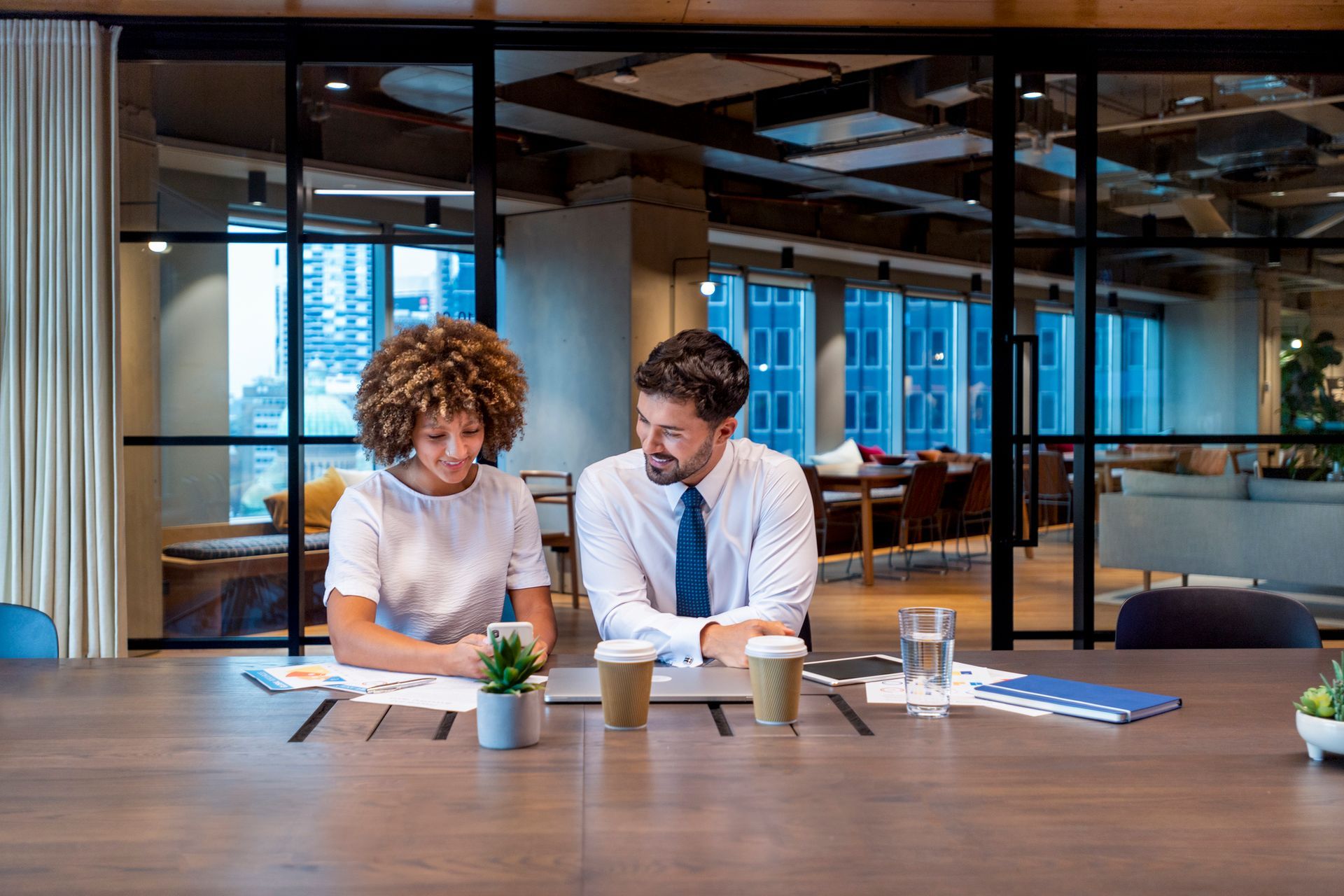 A man and a woman are sitting at a table looking at a laptop.