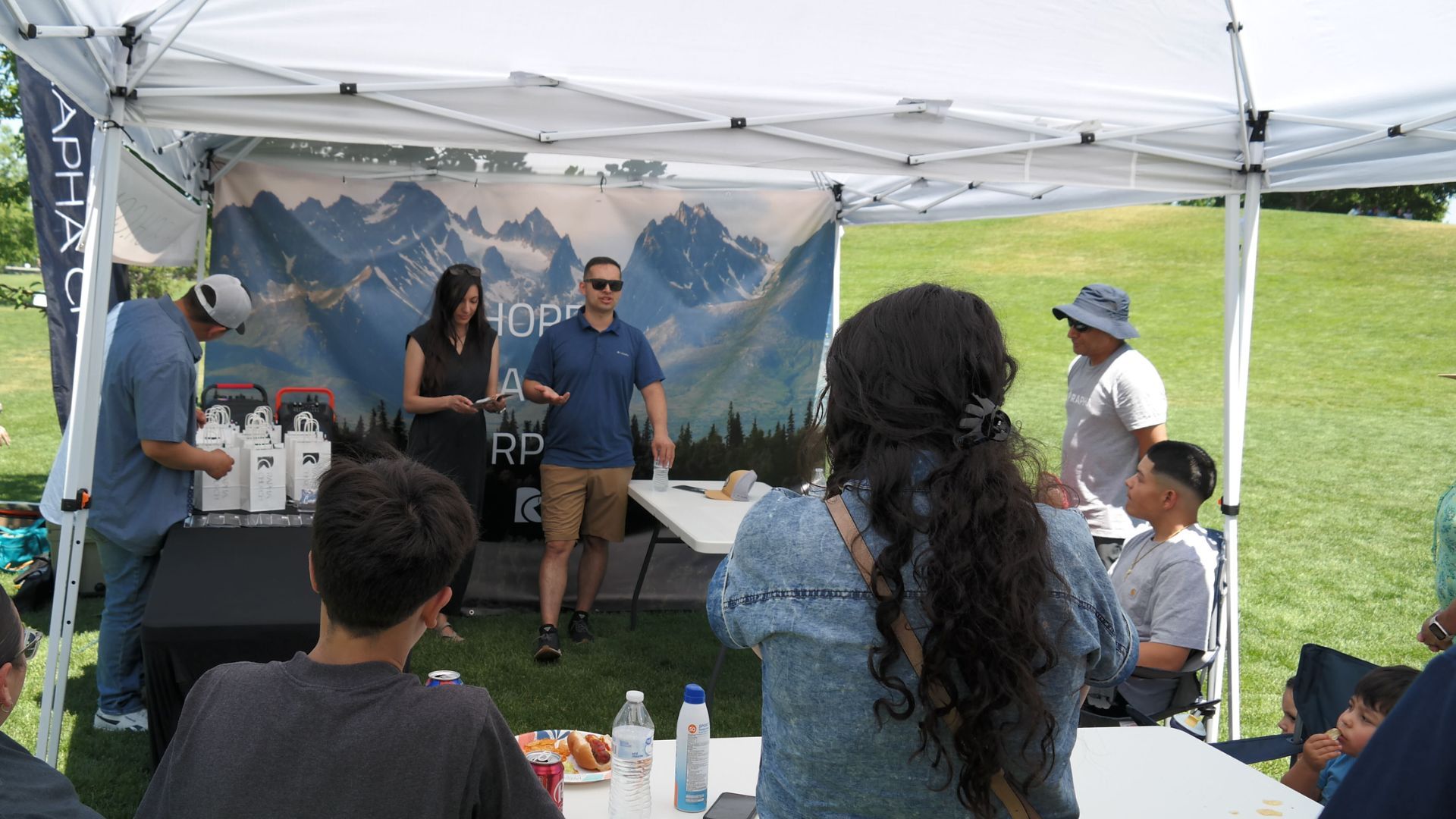 A group of people are sitting under a tent in a park.