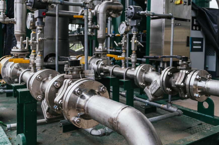 Tubazioni e valvole industriali in acciaio inossidabile in un contesto industriale, con grandi tubi di collegamento e supporti metallici.
