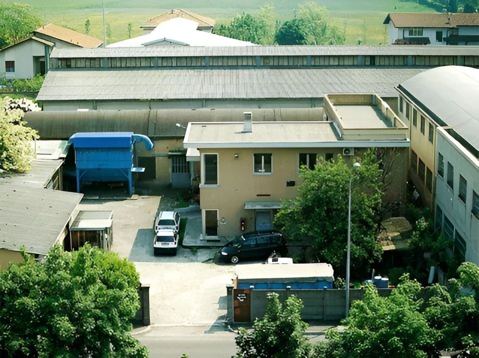 Veduta aerea di un complesso residenziale con edifici color beige, alberi, auto parcheggiate e un camion blu.