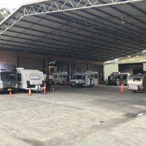 A row of rvs parked under a canopy in a parking lot.