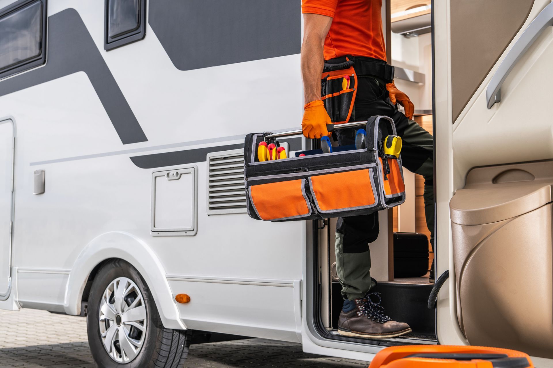 A man is getting out of a rv with a tool bag.