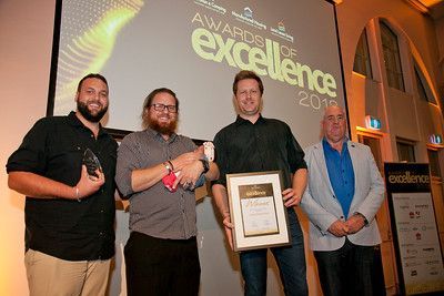 A group of men are standing in front of a large screen holding awards.