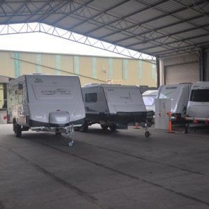 A row of trailers are parked in a garage under a roof.