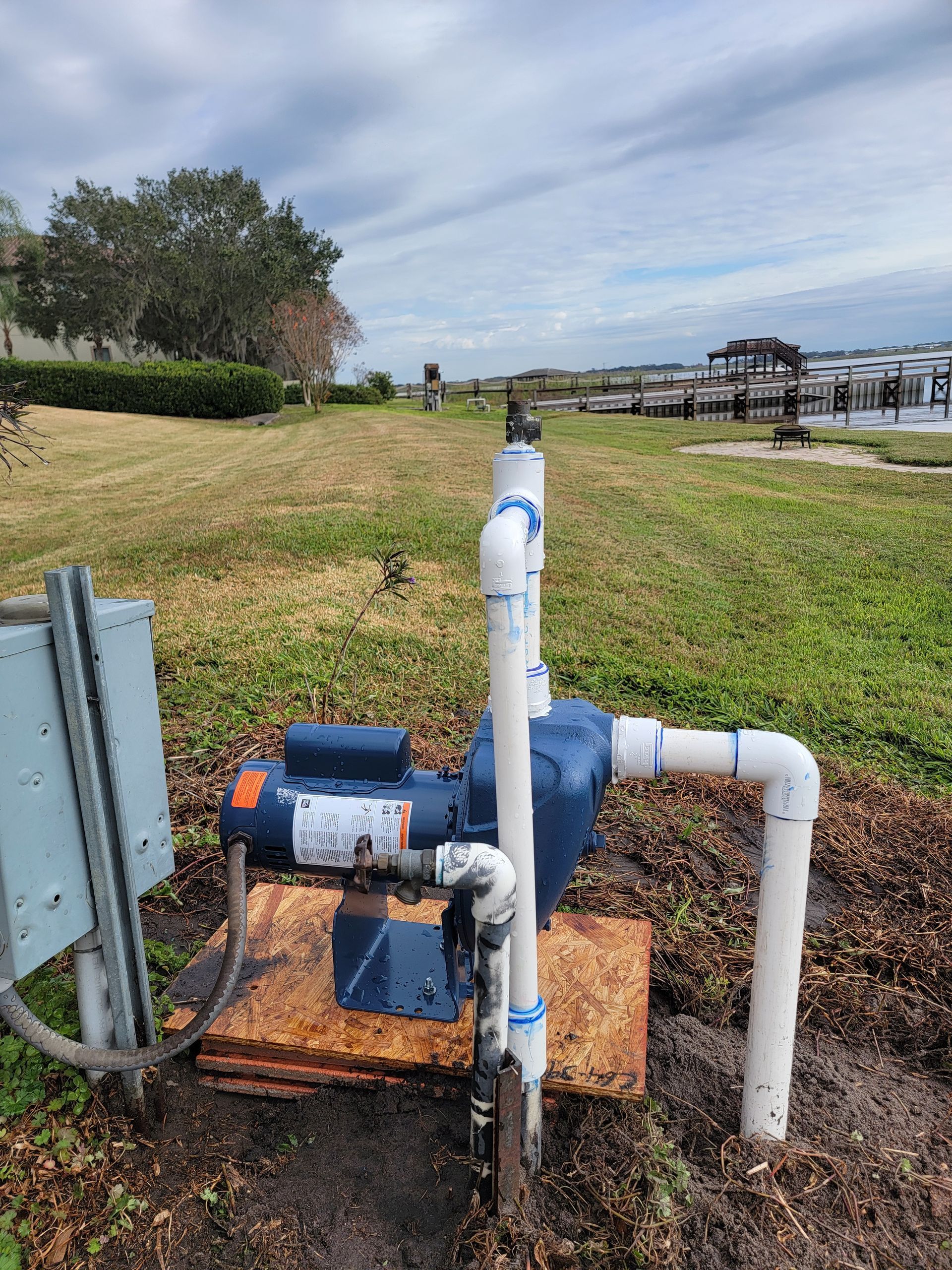 Blue and white pipe valves beside a grassy field and walking path under a cloudy sky