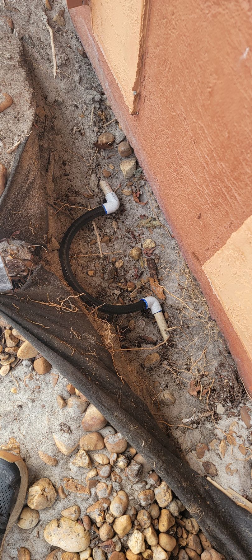 Close-up of a cracked wall base with exposed dirt, rubble, and a black plastic barrier.