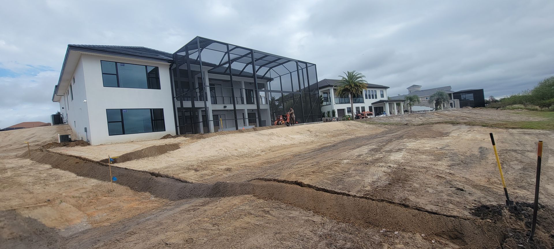 Modern building under construction beside a muddy dirt lot under cloudy skies