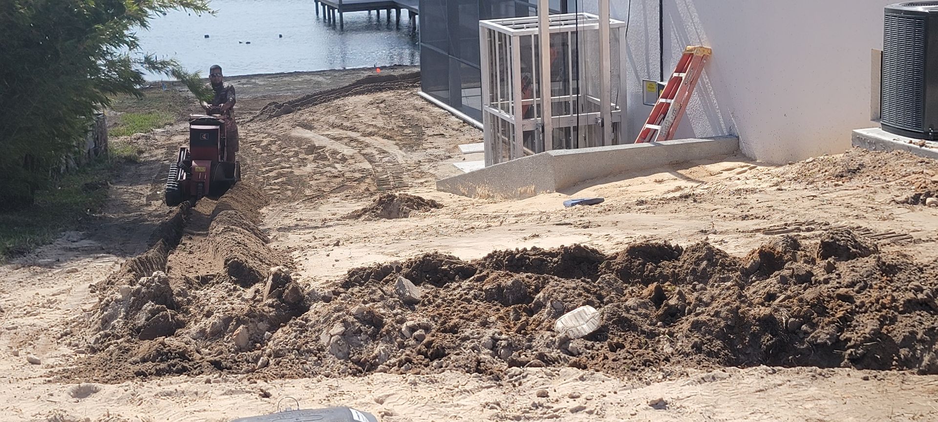 Construction site beside water with muddy ground, excavator, and building materials near a concrete structure