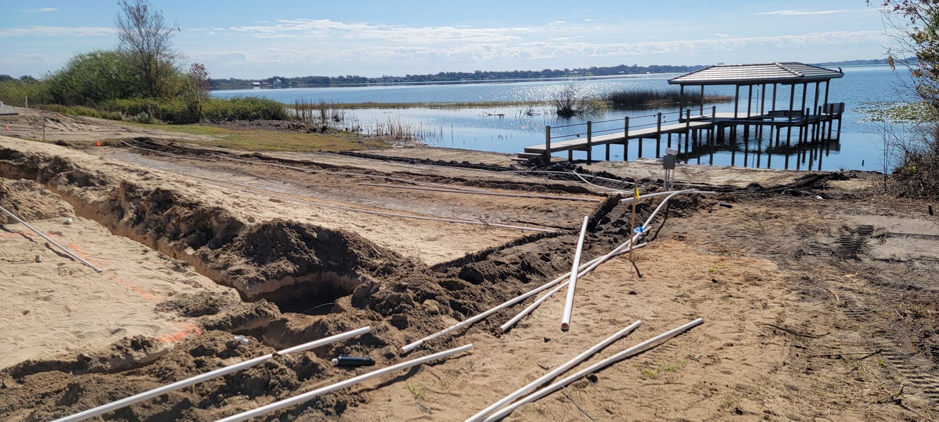 Damaged sandy shoreline with broken wooden dock extending into calm water under clear skies