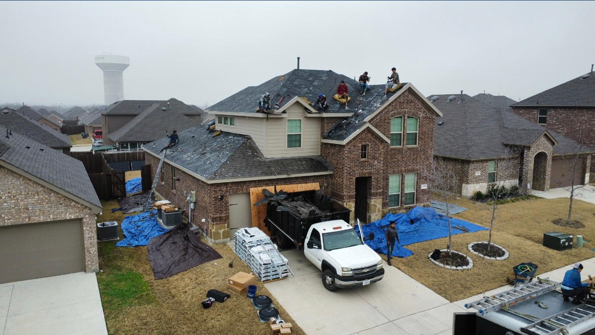 A residential home with a partially replaced roof, featuring a white truck in the driveway and workers on the roof.