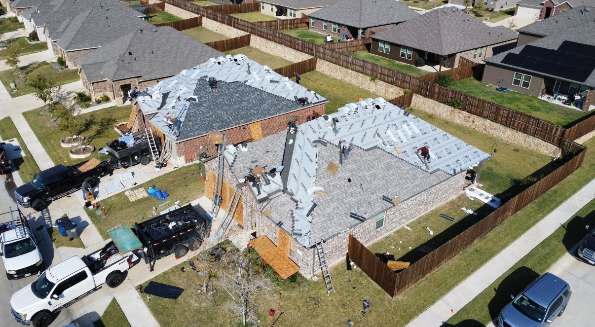 Aerial view of two suburban houses undergoing roof replacement with roofing materials, dumpsters, and trucks in the driveways.