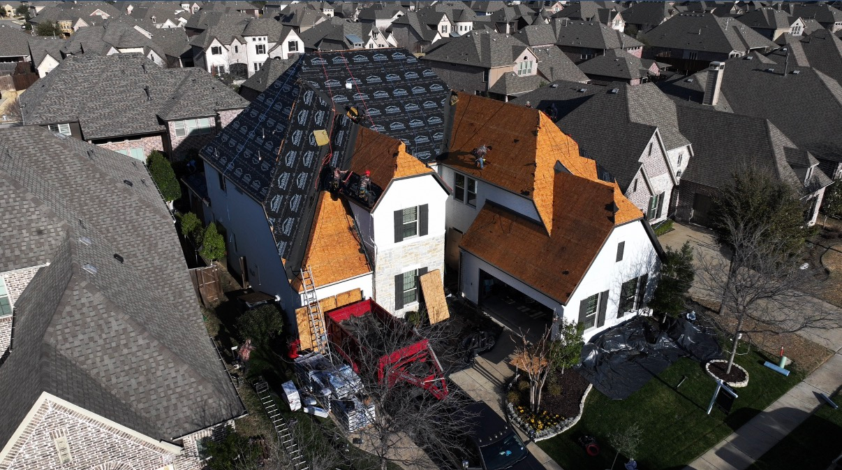 An aerial view of a suburban house under construction, with a partially replaced roof and materials in the driveway.