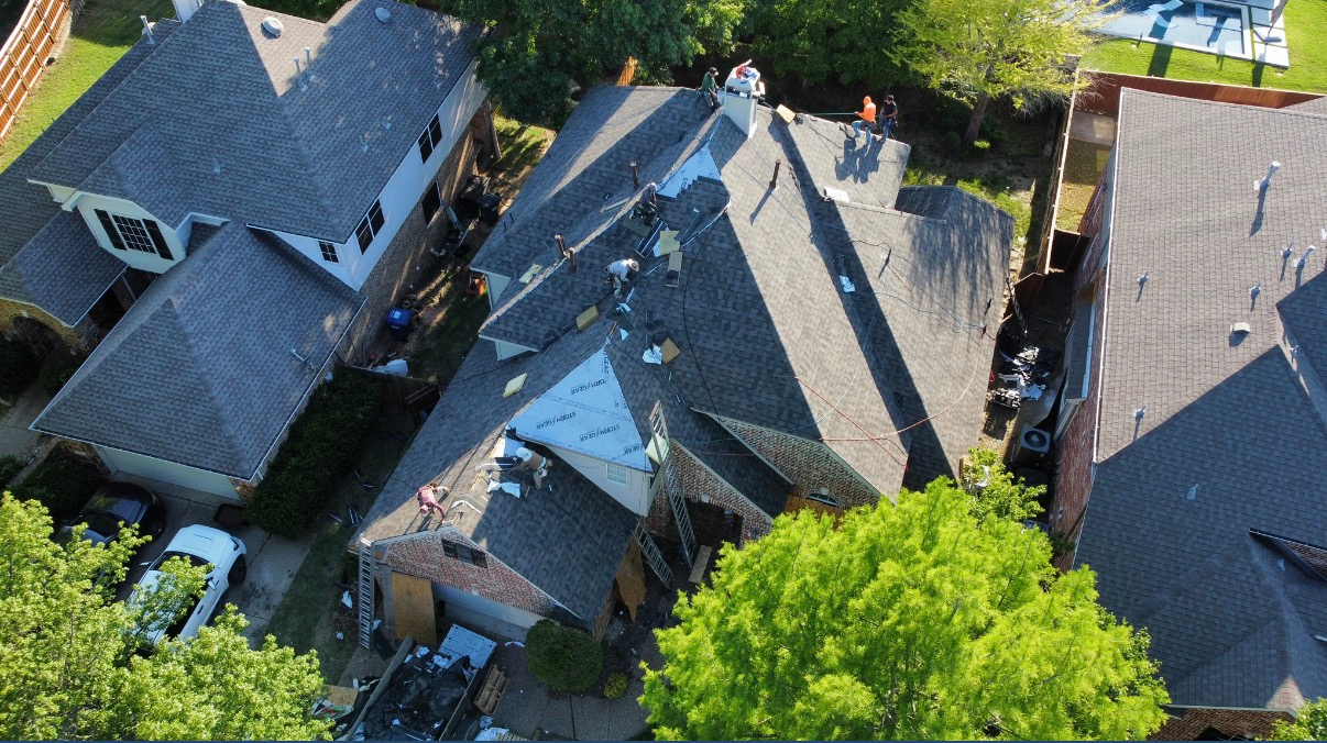 Aerial view of workers replacing shingles on a house roof in a suburban neighborhood.