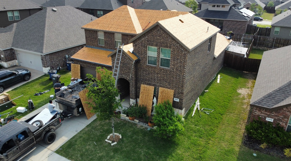 Aerial view of a brown brick house under construction with new wooden roof decking and a truck parked in the driveway.
