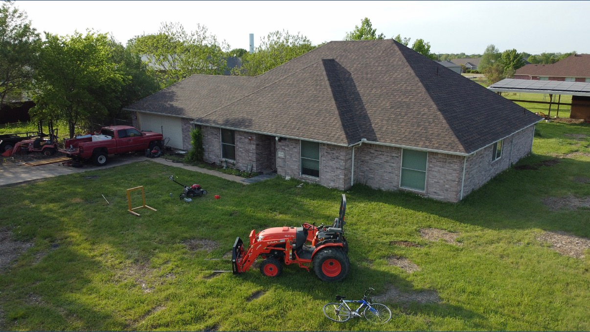 Aerial view of a suburban brick house with a red pickup truck and an orange tractor in the lawn.