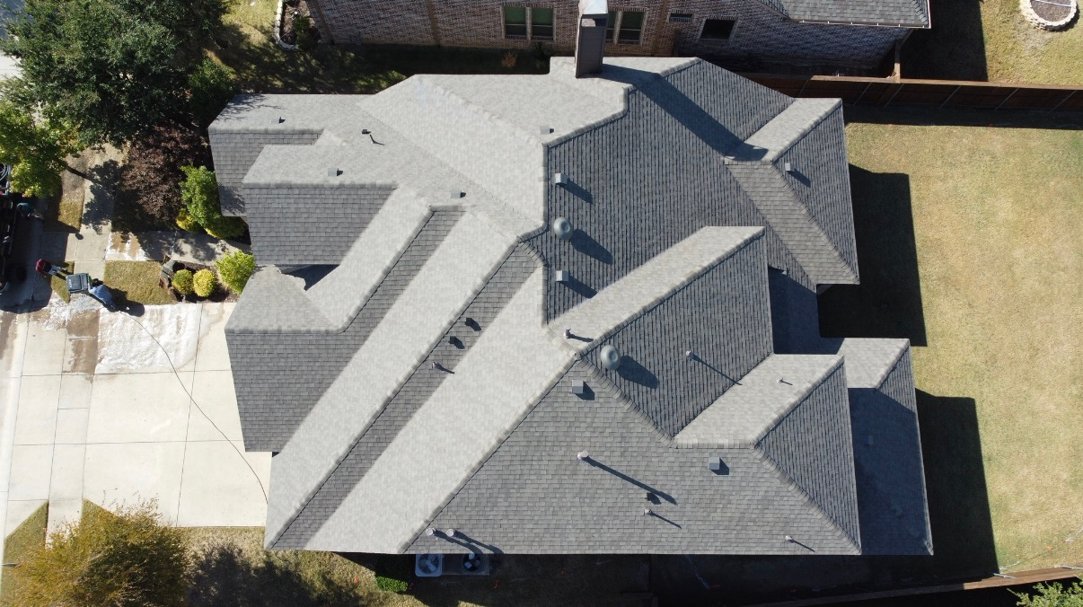 A top-down aerial view of a gray shingled residential roof with multiple peaks and a chimney.