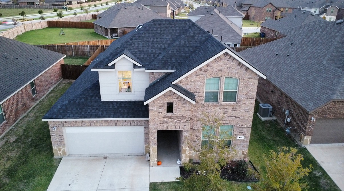 An aerial view of a two-story brick suburban house with a dark roof and a two-car garage.