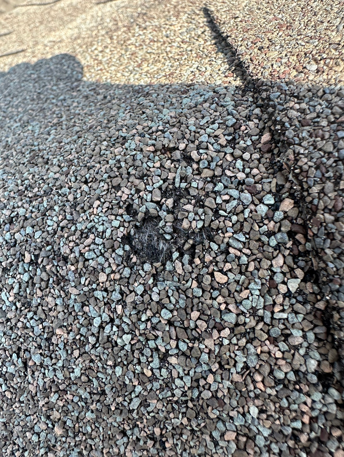 A close-up view of grey and brown gravel with a distinct black line running through the center of the stones.