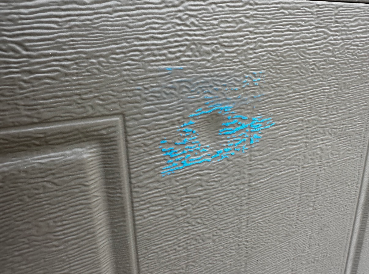 A textured, light gray surface featuring a shallow, round dent surrounded by bright blue paint transfer.