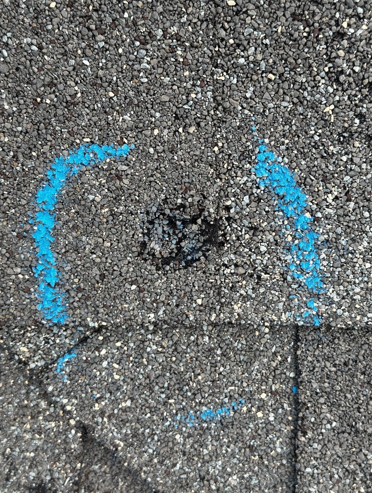 A small patch of asphalt marked by two curved blue chalk lines, framing a rough, dark spot in the center.