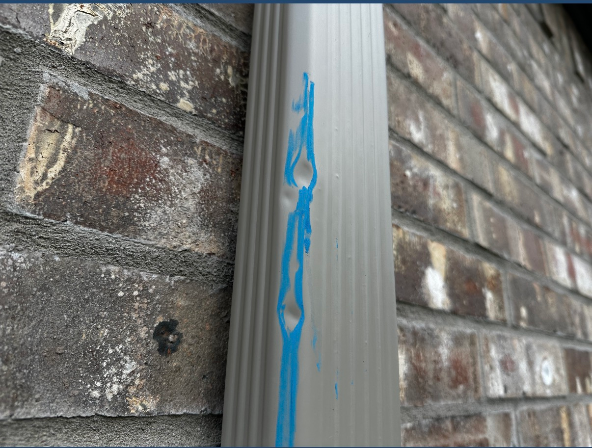 A grey downspout against a brick wall with two small dents highlighted by bright blue paint.