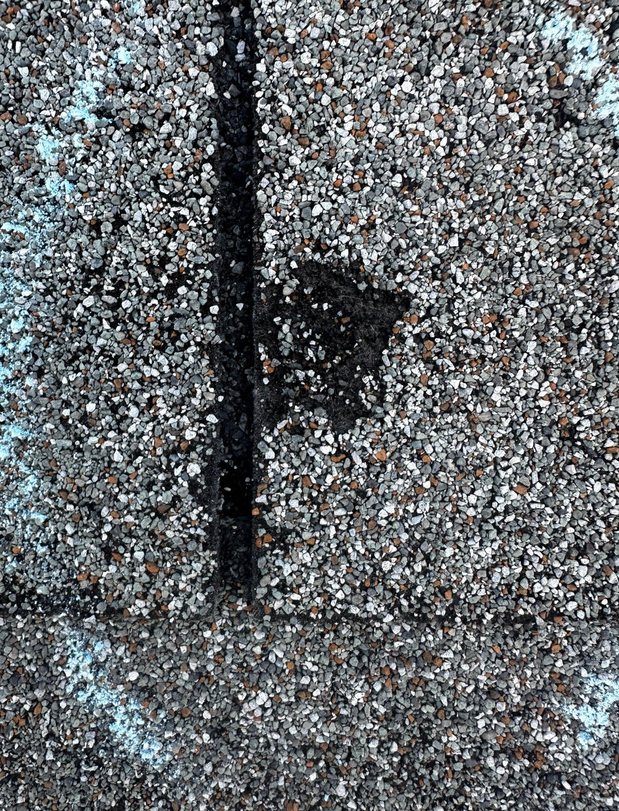 A close-up of a damaged gray asphalt roof shingle showing granule loss and a circular mark from a chalk inspection.