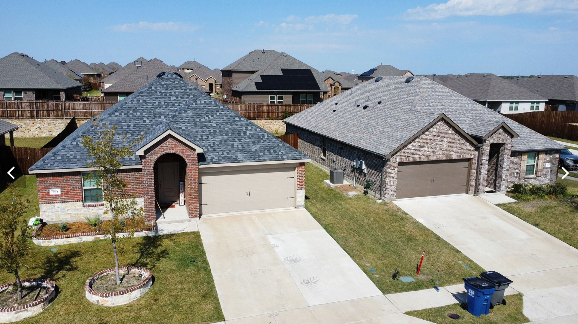 An aerial view of two adjacent single-story brick suburban homes with concrete driveways on a sunny day.