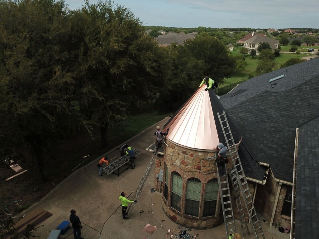 Construction workers on a house roof installing copper roofing, ladders, and safety gear.