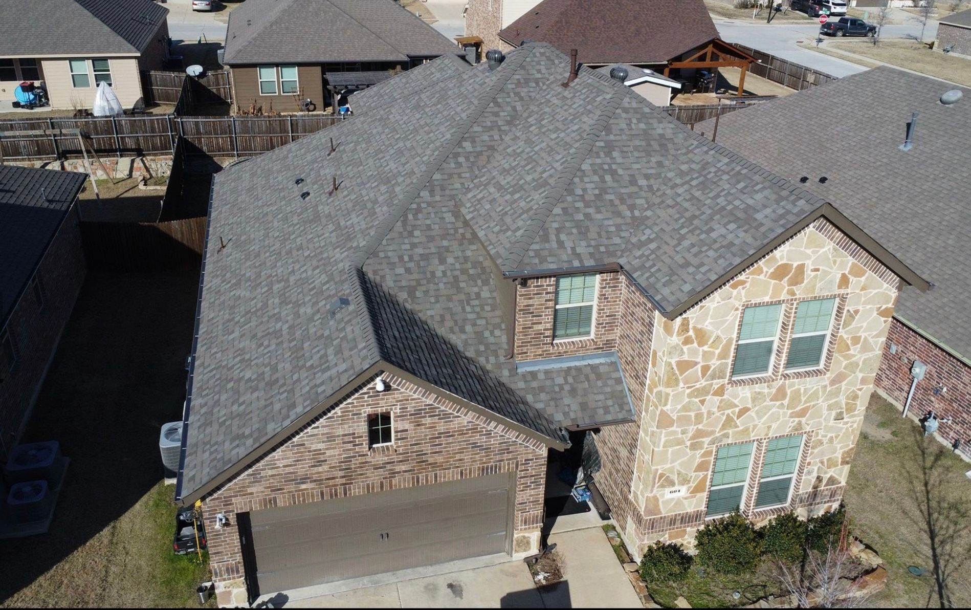 Two-story house with stone facade and gray roof in a suburban neighborhood.