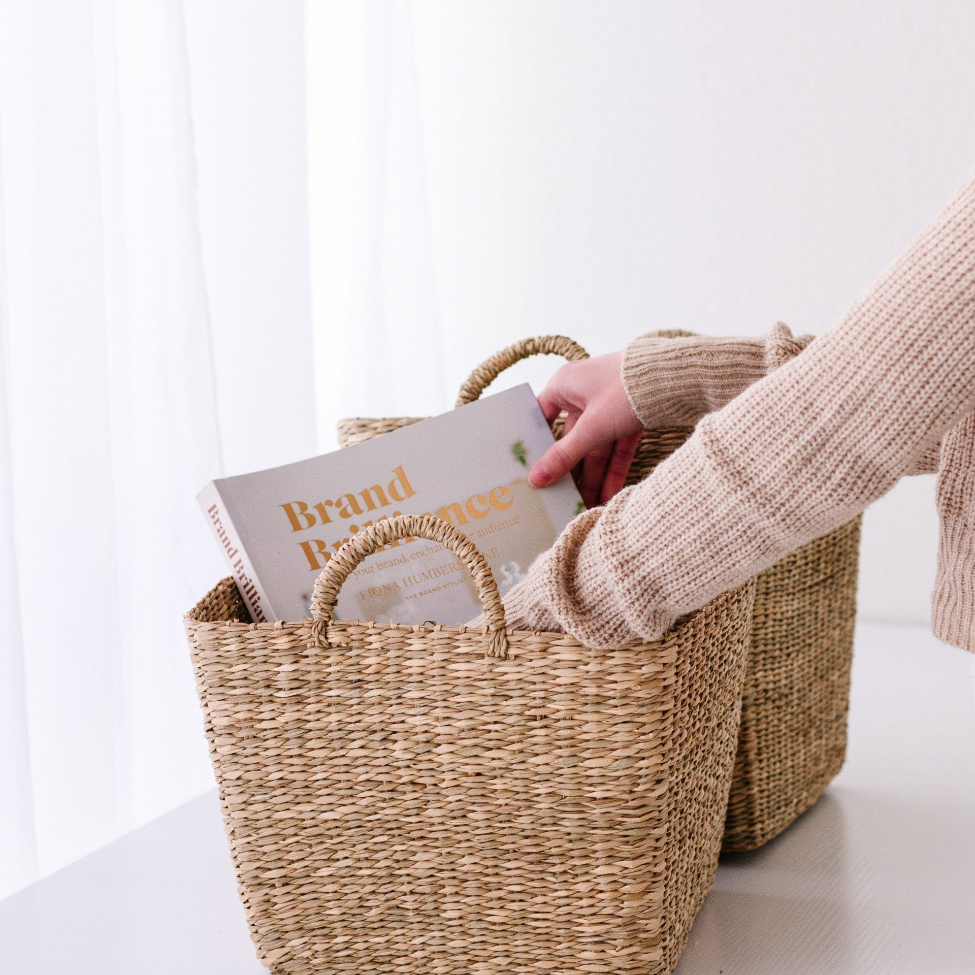 A person is holding a wicker basket with a book in it.