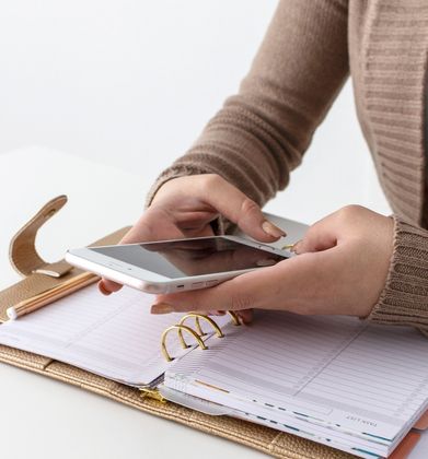 A woman is holding a cell phone over a notebook