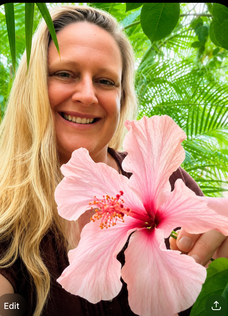 Smiling woman in a white sleeveless top against a lush green outdoor background