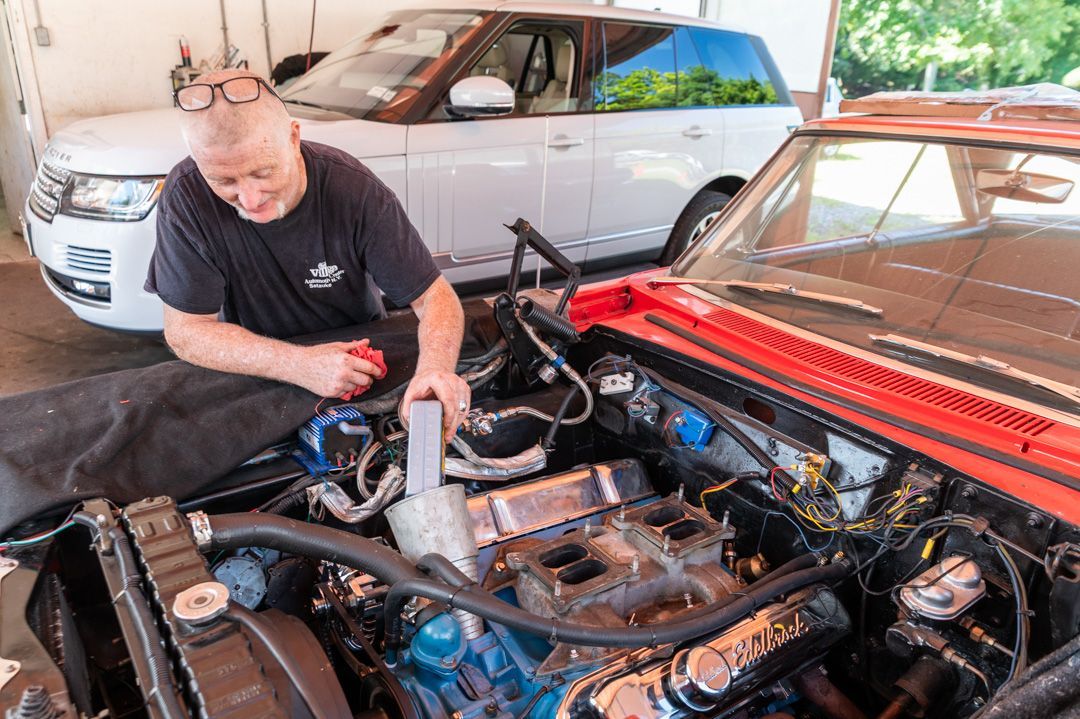 Mechanic working on car engine, using a wrench. Hands wear gloves. Orange cable visible.