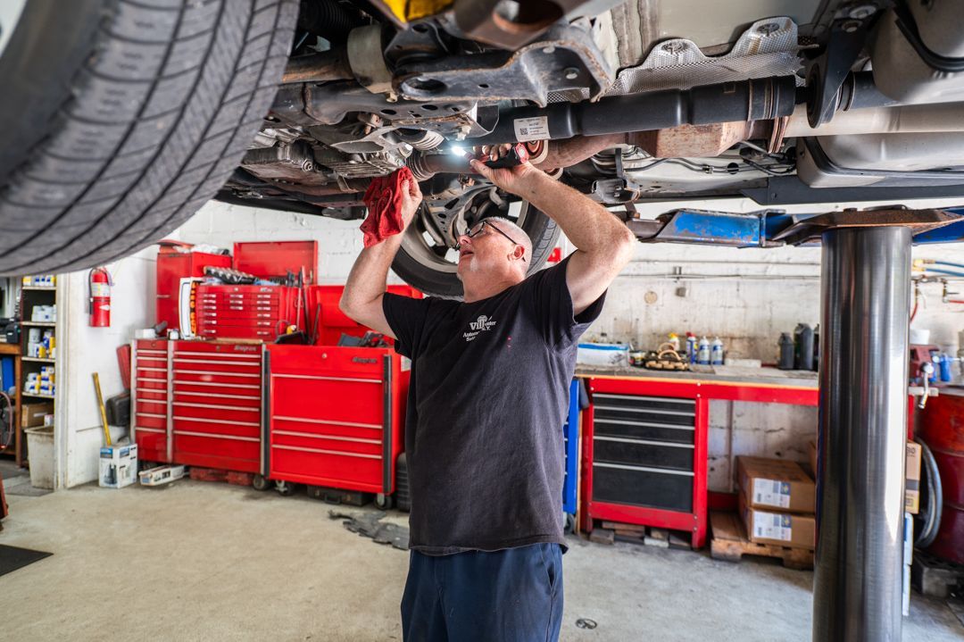 Mechanic inspecting a car’s undercarriage in a garage with red tool cabinets.