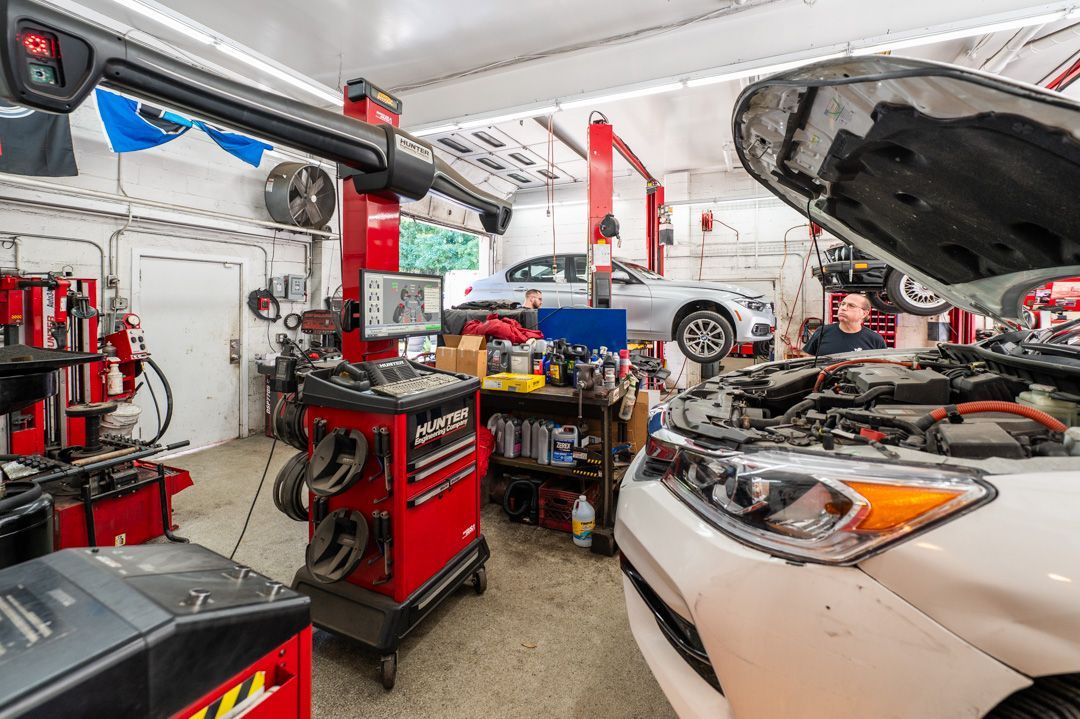 Auto repair shop with a white car on a lift, open hood, red tool cabinets, and assorted equipment