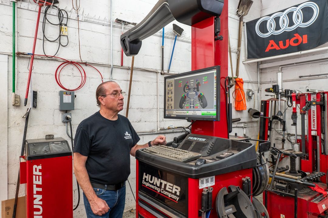 Mechanic in an auto shop beside a Hunter wheel aligner and Audi sign, viewing a monitor.