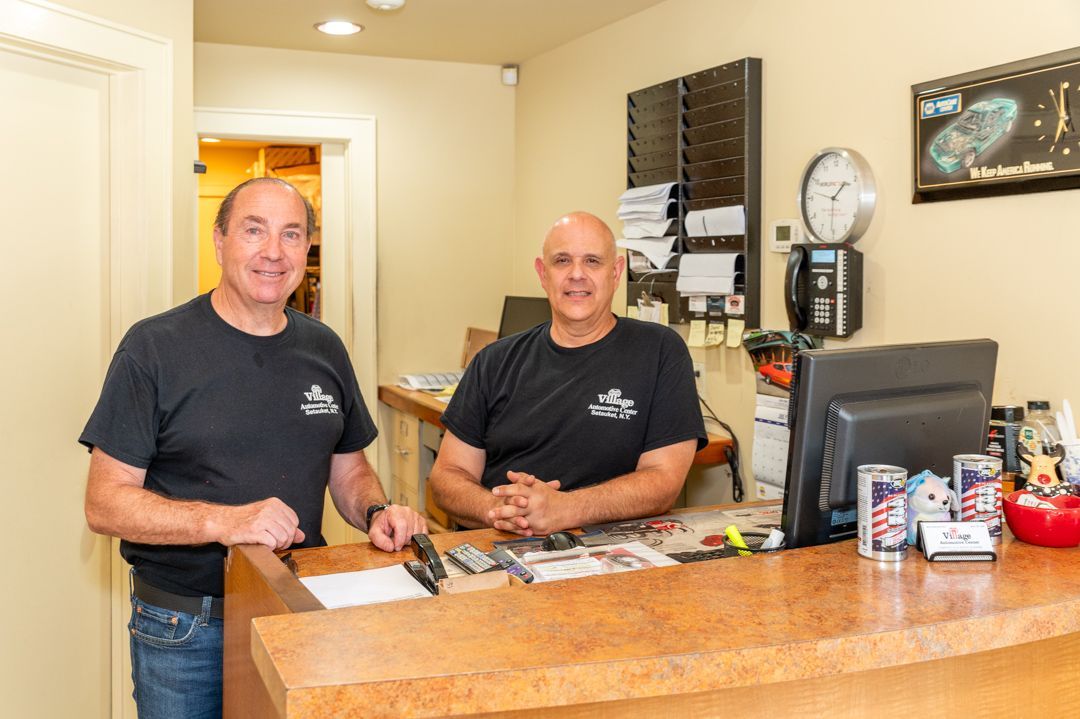 Three men stand behind a counter in an office. They smile, one wearing jeans, the others black shirts.