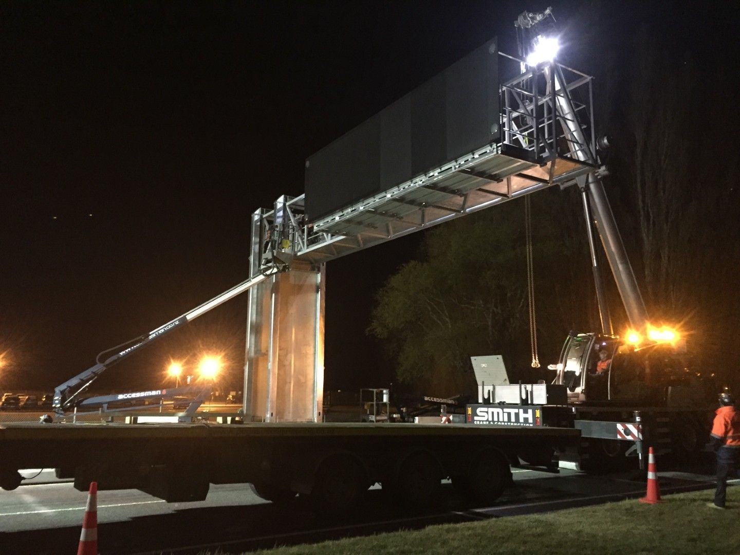 A large billboard is being lifted by a crane at night
