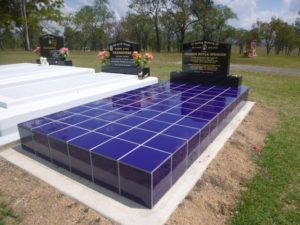 Blue-tiled grave site with headstone, concrete border, and other graves in background, under a blue sky.